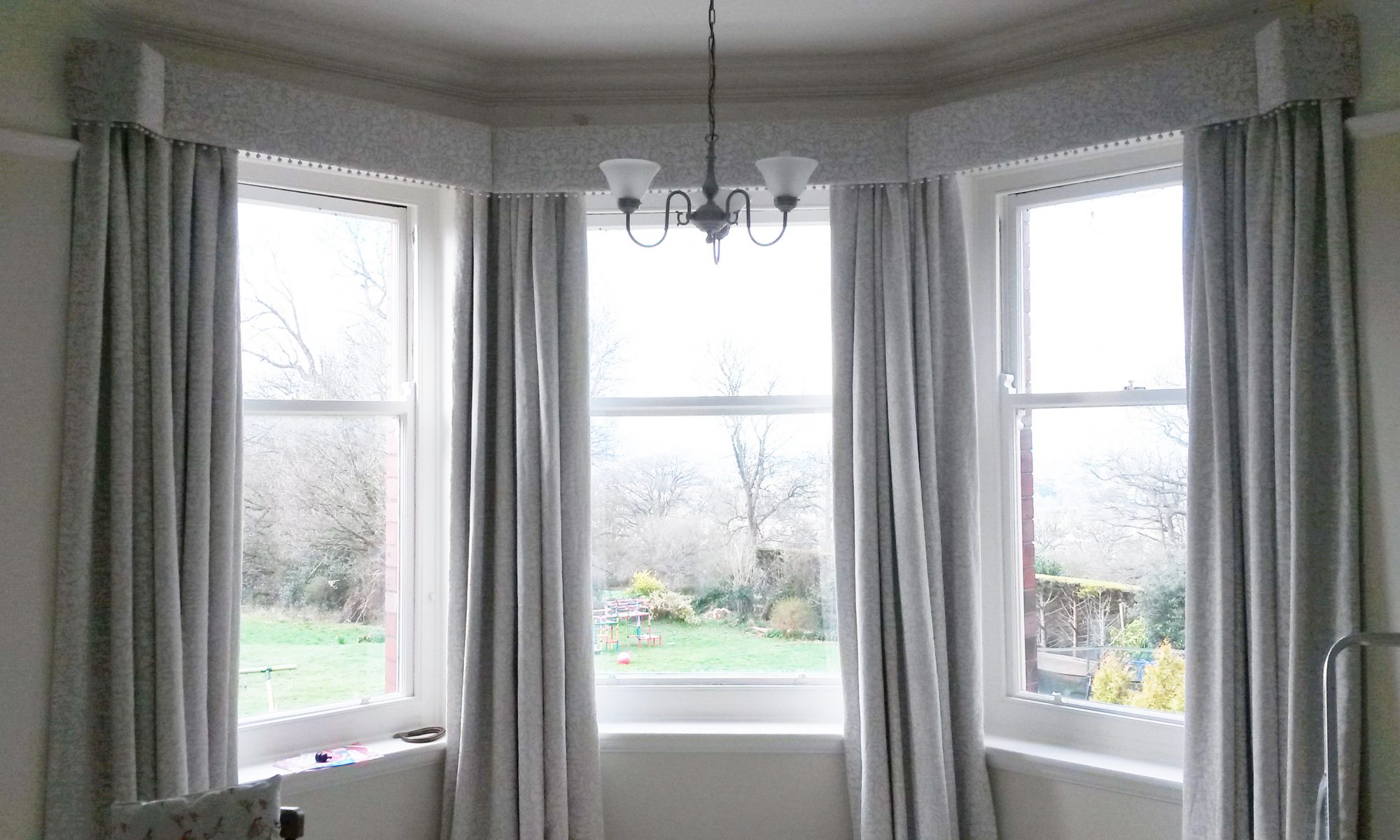 Straight pelmet with pop pom trim in bay window. Morris and Co Pure fabric