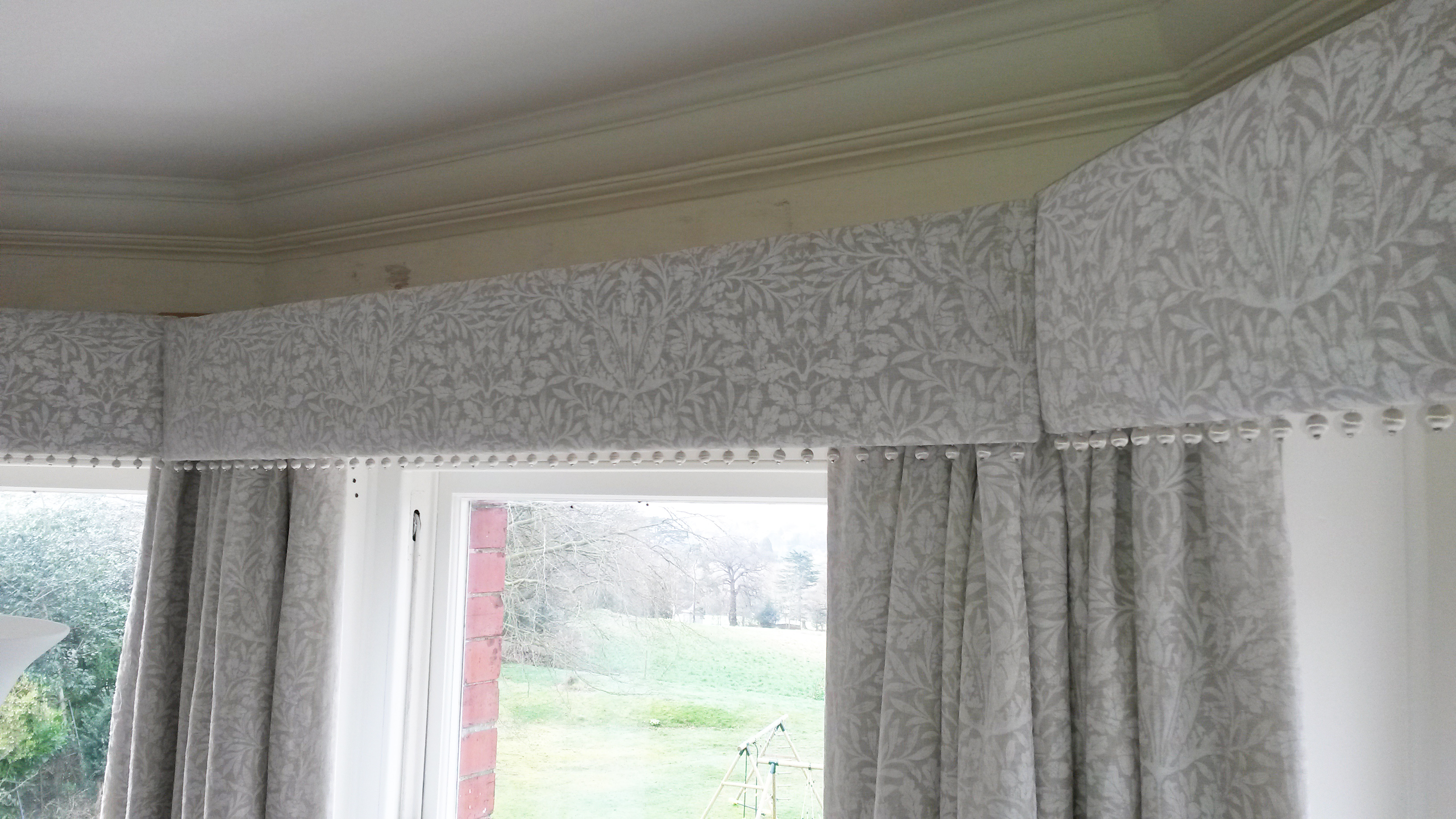 Straight pelmet with pop pom trim in bay window. Morris and Co Pure fabric