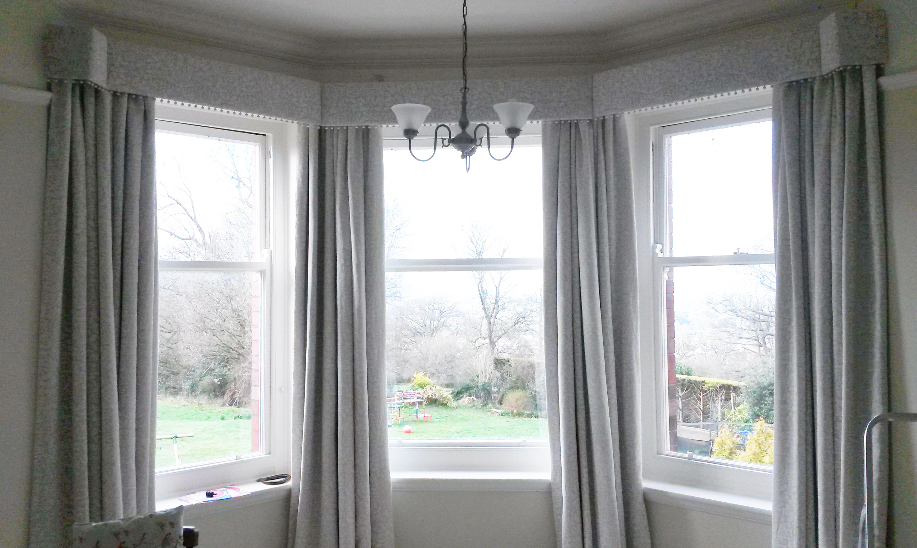 Interlined curtains in bay window with pom pom trim pelmet