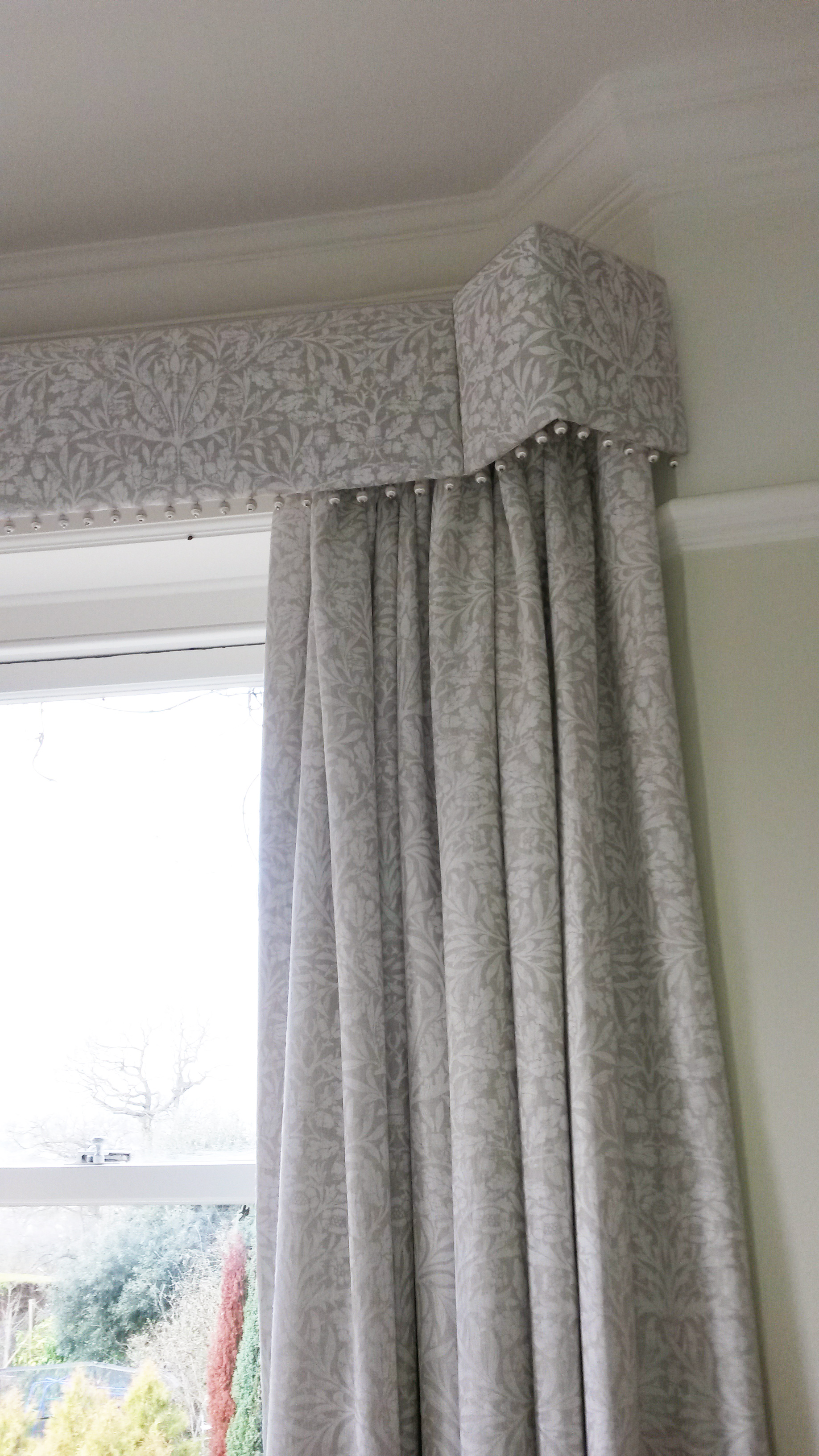 Straight pelmet with pop pom trim in bay window. Morris and Co Pure fabric